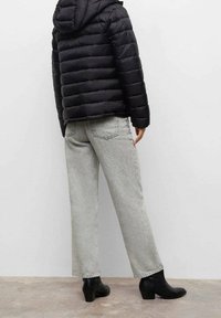 Svart puffjacka med huva, grå vida jeans och svarta ankelboots, visar upp en quiltad textur och en avslappnad silhuett.