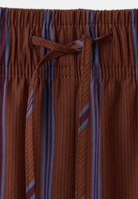 Prim-plan cu material maro cu dungi verticale albastre și roșii, evidențiind o talie elastică și o șnur legat.