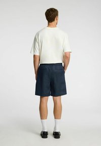 Lys beige kortærmet skjorte med en afslappet pasform, parret med marineblå shorts med elastisk talje og to baglommer.