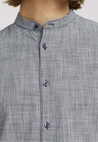 Camisa de cuadros vichy en blanco y negro con cuello mao, que presenta cierres de botón y una tela ligera y texturada.