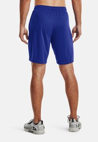 Blaue Sportschorts aus Netzstoff, mit elastischem Bund und knielangem Schnitt. Eine Person trägt graue Turnschuhe mit schwarzen Akzenten.