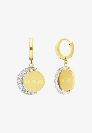 Gold-tone earrings featuring a crescent shape, a smooth surface, and crystal accents with the "GUESS" logo engraved on a circular pendant.