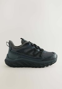 Sort atletisk sneakersko med tykk, robust sål, strukturerede paneler, snørebånd foran og polstret ankelkrave mod en ensfarvet lys baggrund.