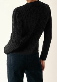 Czarny sweter w splot kraty z okrągłym dekoltem i długimi rękawami, w zestawieniu z ciemnymi spodniami z sztruksu, podkreślającymi fakturę materiału oraz dopasowanie.