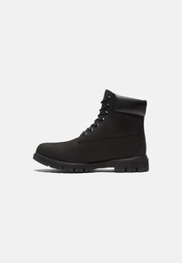 Bottine en cuir noir avec une texture lisse, bout rond, col rembourré et semelle en caoutchouc robuste avec un motif de crampons pour une traction optimale.