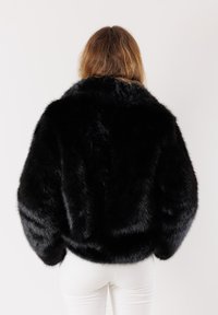 Giacca in faux fur nera con una texture morbida e pelosa, design corto e maniche ampie. Presenta un colletto alto, vista dal retro.