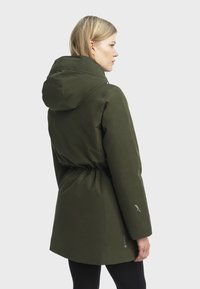 Veste imperméable vert olive avec capuche, taille cintrée et finition lisse. Dotée du logo GORE-TEX sur la manche et d'accents de design subtils.