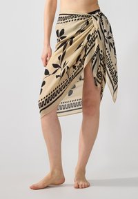 Hame skidi kangasta beige, jossa on mustia kukkakuviota ja geometrisia reunoja. Sidottu vyötärölle ja sivussa on halkio, joka tuo lisää yksityiskohtia.