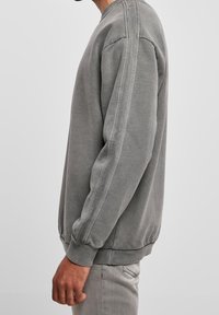 Sudadera gris de cuello redondo con tejido texturizado, puños y dobladillo acanalados. Presenta costuras laterales con detalles sutiles para un diseño adicional.