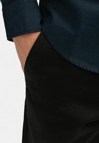 Mörkblå skjorta med knäppt krage och uppvikta ärmar, matchad med svarta byxor. Materialet verkar vara slätt med en ren, åtsittande design.