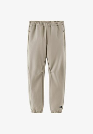 Pantaloni jogger beige a gamba affusolata con vita elastica e polsini, tasche laterali con zip e una piccola patch con logo nero vicino alla caviglia sinistra.