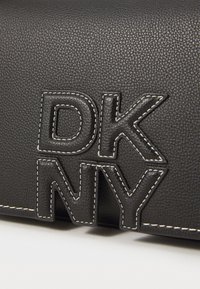 Geantă din piele neagră, cu litere DKNY ridicate dintr-un material texturat, accente de cusături albe contrastante și un finisaj neted.