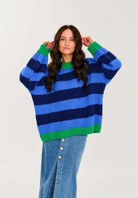 Pletený pruhovaný svetr v modré, námořnické a zelené barvě, s volným střihem a širokými rukávy, zkombinovaný s džínovou sukní s knoflíky.