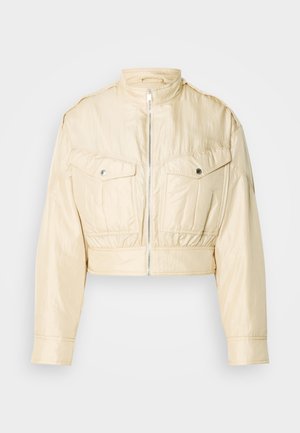 Béžová krátka bunda so zipsom vpredu, stojačikovým golierom, dlhými rukávmi a dvoma zapínacími náprsnými vreckami na jednoduchom pozadí.