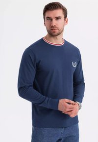 Navy long-sleeve shirt with a round neck featuring red and white striped trim. Small logo on the left chest, made from soft material.