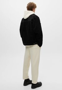 Giacca di velluto a coste nera con una felpa bianca con cappuccio sotto, abbinata a pantaloni della tuta color crema e stivaletti neri alla caviglia.
