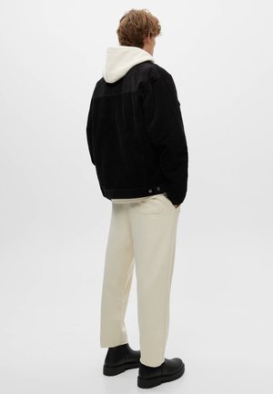 Giacca di velluto a coste nera con una felpa bianca con cappuccio sotto, abbinata a pantaloni della tuta color crema e stivaletti neri alla caviglia.