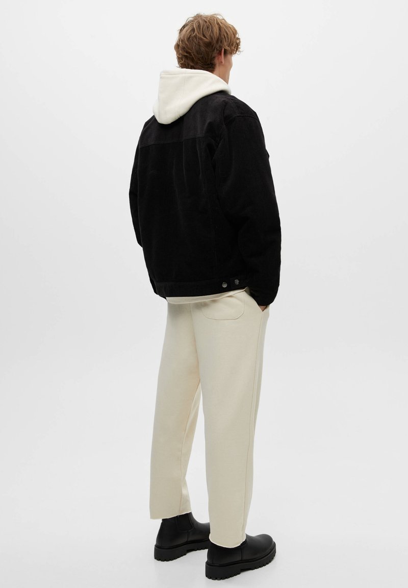 Giacca di velluto a coste nera con una felpa bianca con cappuccio sotto, abbinata a pantaloni della tuta color crema e stivaletti neri alla caviglia.