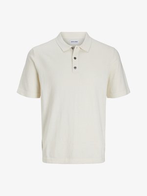 Polo shirt blanc à manches courtes en tissu doux et texturé, avec un col et trois boutons foncés sur le plastron.