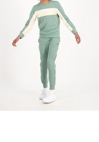 Sudadera verde menta y joggers a juego con acentos color crema. Presenta puños acanalados y un logo en el pecho. Combinado con zapatillas blancas.