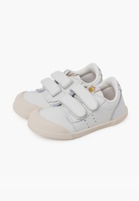 Zapatillas blancas de cuero con dos correas de Velcro, punta redondeada y suela de goma texturizada. Pequeño logo decorativo en el lateral.