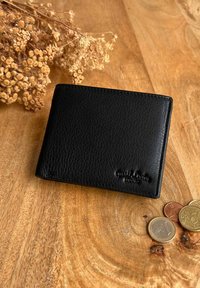 Czarny skórzany portfel o fakturowanej powierzchni. Posiada prosty design i wytłoczone logo. Obok, rozrzucone monety w różnych rozmiarach.