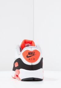 Nike Air-sneakern har en grå mesh-överdela med svarta accenter och ljusa orange detaljer på hälen och logotypen. Texturerad sula med synlig luftkammare.
