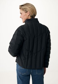 Schwarze Daunenjacke mit vertikalem Steppmuster, hohem Kragen und taillierter Passform. Kombiniert mit blauen Jeans, die einen lässigen Stil zur Schau stellen.