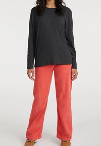 Schwarzes Langarmoberteil kombiniert mit lockeren, gerippten korallenfarbenen Hosen, die einen entspannten Schnitt und eine glatte Textur für Komfort bieten.