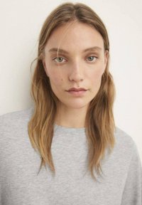 Grå sweatshirt med rund halsudskæring, blød tekstur og afslappet pasform, båret af en person med glat, mellemlangt hår.