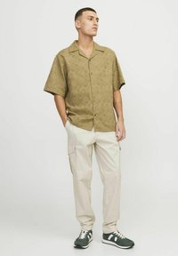 Camisa de manga corta, con cuello abierto y estampado de olivo, combinada con pantalones cargo beige claros y zapatillas verdes con acentos blancos.