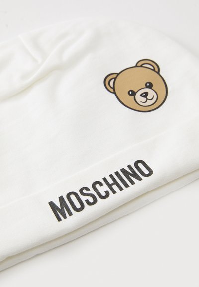 Weißer Stoff mit einem braunen Teddybärgesicht-Print und dem Text "MOSCHINO" in fetten schwarzen Buchstaben am Rand.