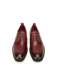 Brązowe skórzane buty eleganckie o gładkiej fakturze, zaokrąglonym nosku i dekoracyjnym sznurowaniu. Posiadają kontrastowy, teksturowany brązowy górny panel.