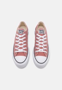 Baskets en toile rose avec lacets blancs, embout en caoutchouc noir et semelle blanche. Présente un logo Converse All Star classique sur la languette.