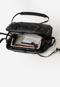 Borsa in pelle nera con apertura a pattina, dotata di un interno a righe e inserti rossi. Include una pochette con zip staccabile e una tracolla regolabile.