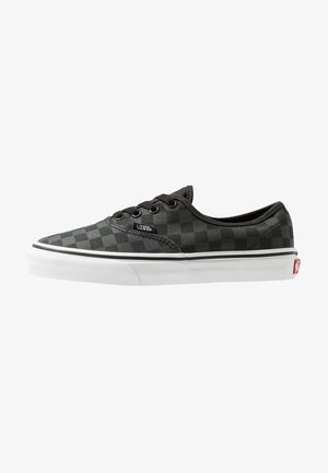 Zapatilla baja Vans de cuadros negros y gris oscuro con suela de goma blanca y ojales negros, etiqueta de logo lateral y tab atrás rojo.