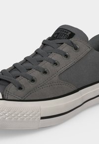 Γκρι χαμηλό sneaker Converse με υφασμάτινη υφή και πάνελ από σουέντ, μαύρο λογότυπο, κορδόνια και λευκή λαστιχένια σόλα με μαύρη ρίγα.