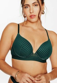 Reggiseno verde scuro con texture a coste, coppe triangolari e scollatura profonda. Presenta spalline sottili e una fascia sotto glitterata.