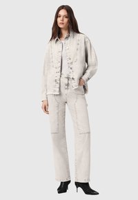 Jasnoszara dżinsowa kurtka z dopasowanymi spodniami, z widocznym szwem i przednimi kieszeniami. Uzupełniona o czarne, wąskie botki za kostkę.