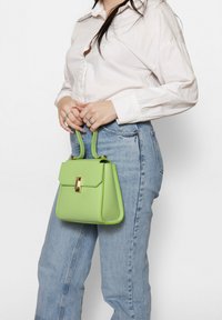 Groene handtas met een gestructureerd ontwerp en een kliksluiting in goudkleur. Gemaakt van glad materiaal met korte handvatten en een hoekige vorm.