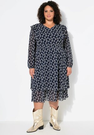 Marineblaues Blumenkleid mit langen durchsichtigen Ärmeln, Rüschendetails, gestaffeltem Design und fließender Silhouette, kombiniert mit metallischen goldenen Cowboystiefeln.
