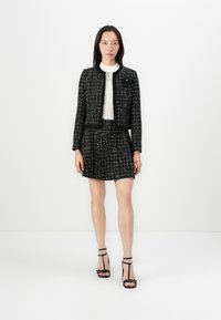 Black and white tweed jacket paired with a matching skirt. Textured fabric with a boxy fit. Model wears a white turtleneck and black strappy heels.