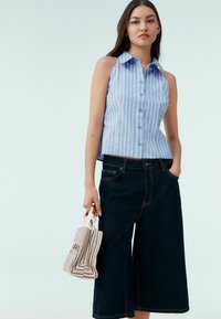 Chemise sans manches rayée bleu clair avec des boutons, associée à un pantalon en jean large et sombre, et portant un sac texturé et rayé.