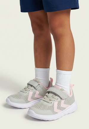Child wearing white socks and gray and pink mesh sneakers with velcro straps, standing on a light background.