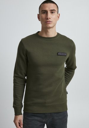 Olive green sweatshirt made of soft fabric, featuring a round neckline and a black logo patch on the chest. Long sleeves and ribbed cuffs.