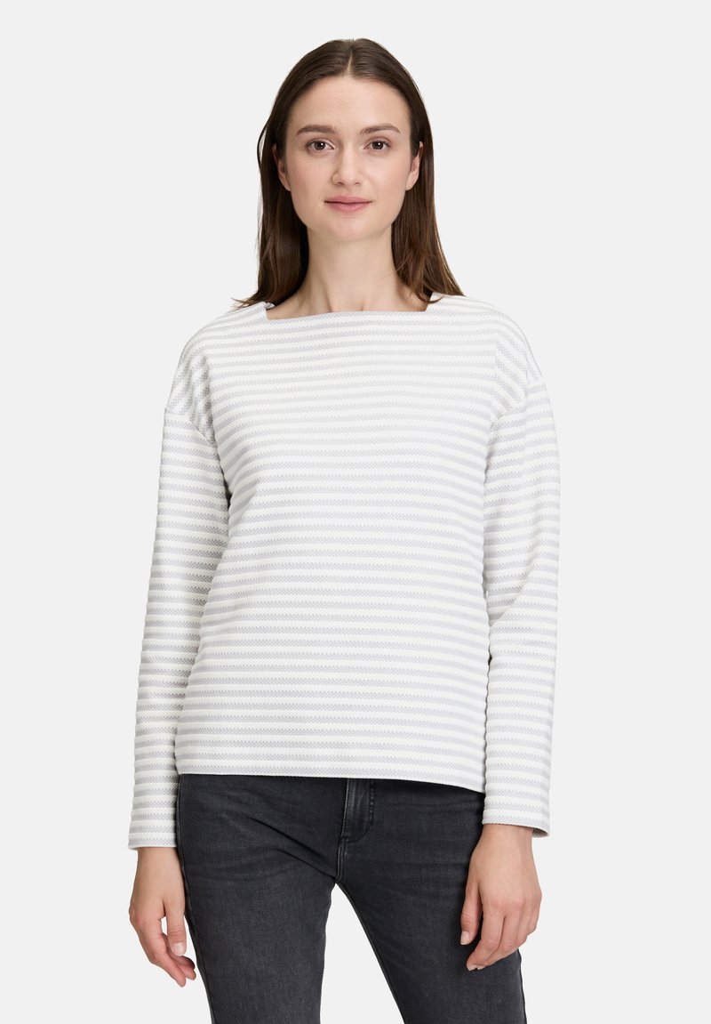 Haut à manches longues rayé en blanc et gris clair, avec un col bateau et une coupe décontractée. Texture douce avec un motif côtelé subtil.