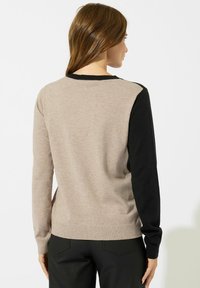 Maglione beige e nero con maniche lunghe, caratterizzato da un design a tinta unita e polsini a coste. Texture morbida con blocchi di colore contrastanti sulle maniche.
