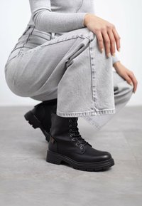 Stivaletti neri con lacci alla caviglia e suola spessa, finitura in pelle liscia e occhielli in metallo. Indossati con jeans grigi a vita alta.