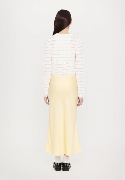 White long-sleeve top with textured stripes, paired with a yellow, ankle-length skirt. The outfit is completed with black shoes and white socks.
