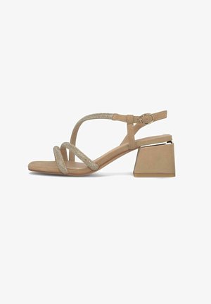 Sandale beige à bout ouvert avec des brides croisées ornées de strass, une boucle à la cheville, et un talon bas et épais sur fond blanc.